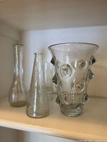 Three clear glass vases on shelf including Barovier Mugnoni, ribbed long-neck vase, and conical bubble vase