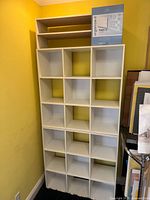 Full view of tall white cubby shelving unit against yellow wall