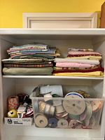 Shelf with folded vintage fabric pieces and clear bin of ribbons and trim