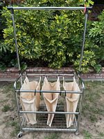 Full view of chrome laundry sorter cart with three canvas bags and garment bar outdoors