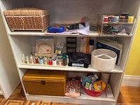 Three shelves showing two sewing baskets, thread rack, pin dish, thread caddy, organizers and notions