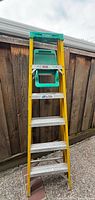 Full front view of yellow fiberglass step ladder with green top cap and aluminum steps