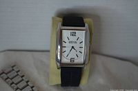 Front view of the watch showing rectangular case, white dial, black strap