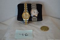 Front view of both Citizen watches on cushion with coin for scale