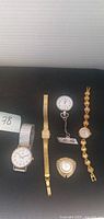 Group shot of all five items: two wristwatches, pendant watch, nurse watch, bracelet