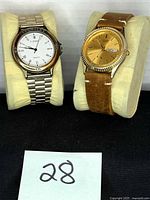 Front view showing Cote d’Azur silver watch and gold-tone fluted-bezel watch on cushions