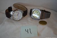 Both wristwatches side by side with coin for scale