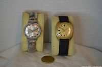 Front view of both wristwatches on cushions with coin for scale