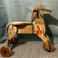 Left side view of antique wooden ride-on horse showing paint details and wheels