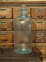 Front view of large aqua glass apothecary bottle with stopper