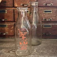 Two glass milk bottles on surface, one printed, one plain