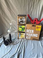 All items together: glass jug, tubing, black stand, Beer Making Kit box with red bottle capper, three visible mix boxes