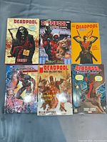 Front covers of all six Deadpool hardcover graphic novels displayed on flat surface