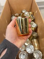 Hand holding a single gold glass votive over box of additional votives