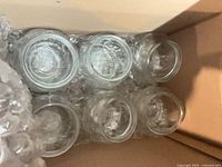 Six clear round glass vases cushioned in bubble wrap inside a box