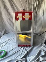 Front view of red and white popcorn machine, marquee reads Pop Corn