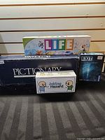 Group shot of all four boxed games: The Game of Life, Pictionary, Joking Hazard, Exit: The Game