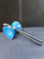 Blue plastic diabolo with attached string and black control sticks on black backdrop