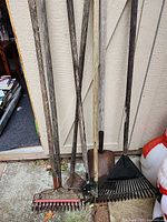 Group of five long-handled garden tools leaning against wall