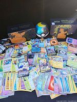 Wide view of scattered Pokémon cards, two storage boxes, Ultra Ball container, pins and coins