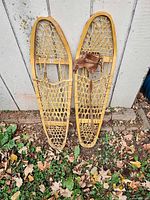 Full view of both wooden snowshoes showing rawhide webbing and one missing strap