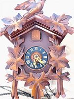 Front view of carved cuckoo clock showing dial, leafy carvings and crest bird