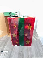 Large red translucent gift box with green ribbon and star motifs, visible internal string lights