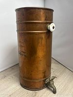 Front view of copper dispenser showing brass spigot and ceramic side mount