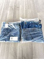 Two pairs of Lee jeans sealed in plastic packaging on floor