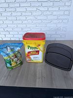 Three lawn care items on table: Preen tub, Impact Organics plant food bag, Suncast hose hanger