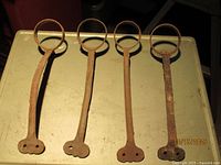 Four cast iron brackets laid flat showing tops and rings