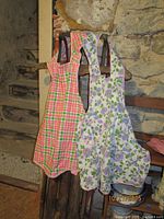 Two full-length aprons hanging, showing gingham and floral patterns