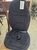 Full view of black seat massage cushion on chair with remote and adapter