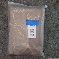 Front view of sealed tan quilted coverlet in plastic bag