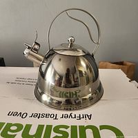 Front view of stainless steel tea kettle showing dome body, lid knob, handle and whistle spout
