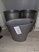 Three waste baskets grouped: grey plastic front, two metal behind