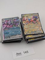 Front view two stacks of sleeved Pokémon EX cards, visible Greninja ex and Koraidon ex