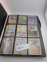 Binder open showing nine Pokémon cards including Mega Ampharos EX, Tapu Koko GX, Guzzlord GX etc.