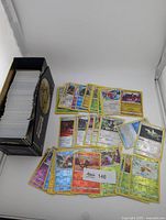 Box filled with stacked Pokémon reverse holo cards and assortment of cards spread out for visibility