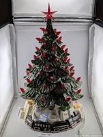 Full view of ceramic Christmas tree with lit red bulbs, star and present/train base