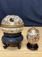Both lidded bowls on their wood stands side by side