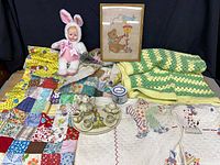 Group shot of all items laid out: three blankets, doll, framed cross-stitch, tea set, money bank