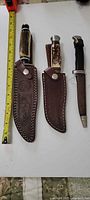 Three knives with sheaths and tape measure for scale