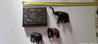Group shot showing carved teak box and three elephant figurines with measuring tape for scale