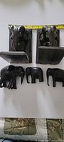 Front view of two carved teak elephant bookends and three carved teak elephant figurines