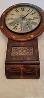 Front view of wall clock showing round dial, inlaid mahogany case and lower box section