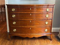 Front view of mahogany serpentine chest showing all four drawers, brass hardware, shaped apron, and feet