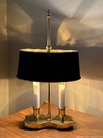 Full view of lit brass bouillotte desk lamp on wooden surface