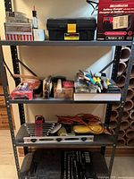 Full shelf showing majority of tool items including toolbox, charger box, tapes, paint brushes, wrenches and extension cord