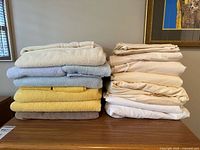 Towels and folded queen sheets stacked on wooden surface